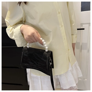 Detail of black hourglass bag with pearl handle and detachable crossbody strap on model