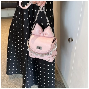 Detail of pink mini handbag with a large bow, silver metal chain, and turn-lock closure