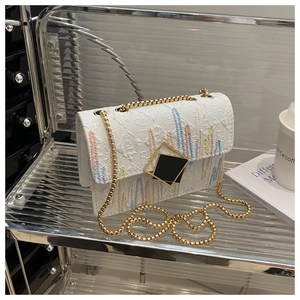 Detail of cream flap bag with colorful striped embroidery and gold sphere chain