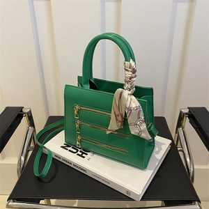 Detail view of green fashion handbag with triple zippers and decorative silk scarf wrap