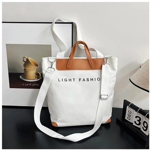 Detail of white canvas tote bag with brown leather handles and LIGHT FASHIO text
