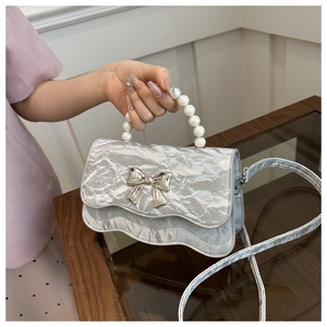 Detail of silver pleated handbag with pearl handle and oversized metal bow clasp