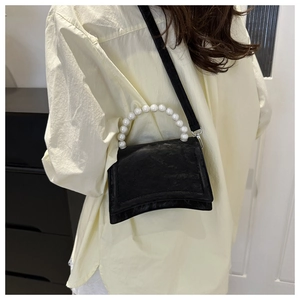 Detail view of black textured handbag with elegant pearl handle and thin shoulder strap