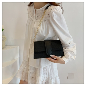 Detail of black rectangular shoulder bag with geometric triangle texture and gold chain strap