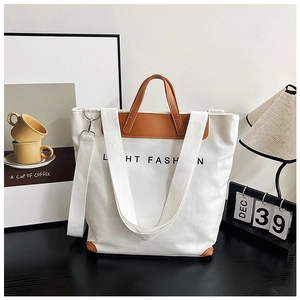 Detail of white canvas tote bag with brown leather handles and adjustable shoulder strap