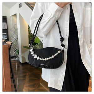 Detail of black crescent shoulder bag featuring pearl heart chain and woven rope strap
