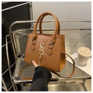 Detailed view of caramel brown tote bag with gold S-buckle and metal tassel charm
