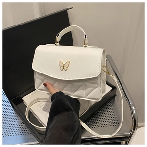 Detail of white quilted crossbody bag featuring a golden butterfly buckle and top handle