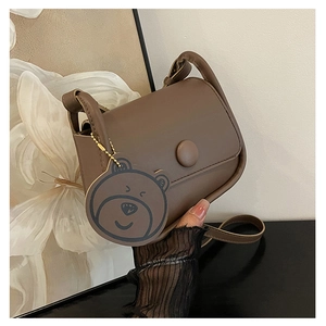 Détail du sac besace en cuir marron mat avec fermeture à bouton et accessoire d'ourson
