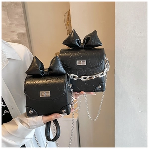 Detail van zwarte tas met strik, zilveren ketting en leer met rimpelige textuur
