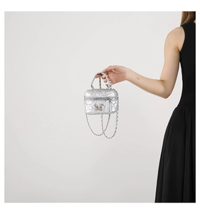 Macro detail of silver quilted mini box bag with metal bow and chain strap on black dress