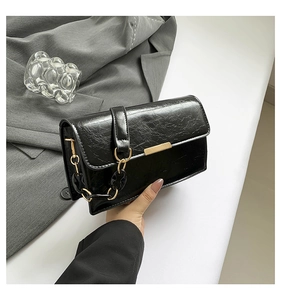 Detail of black pleated faux leather shoulder bag with elegant gold buckle and chain strap