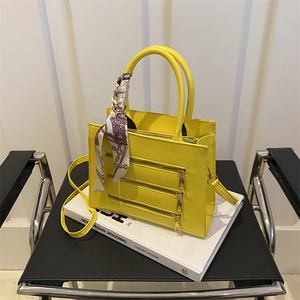 Detail of bright yellow handbag with three golden zippers and silk scarf on handle