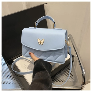 Detail of light blue quilted crossbody bag with decorative white butterfly metal clasp
