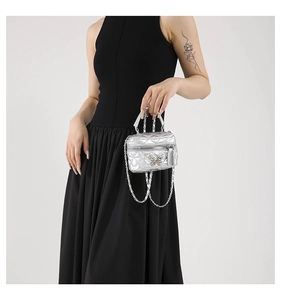 Macro detail of silver quilted mini bag with butterfly metal clasp and chain strap