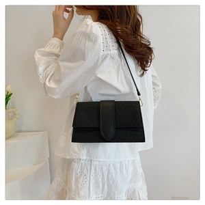 Detail of black geometric embossed crossbody bag with gold hardware on a white lace shirt