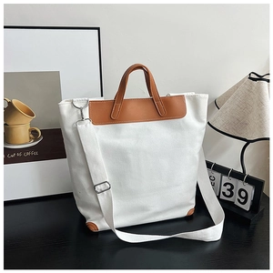 Close-up of canvas tote bag showing dark brown leather handles and silver metal buckles