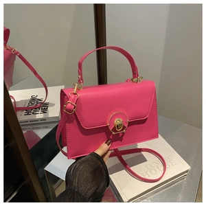 Detailed close-up of rose red leather box bag featuring a golden circular twist-lock clasp
