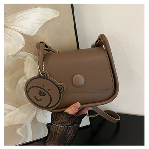 Détail d'un sac besace marron mat avec un charm d'ours mignon et une boucle ronde