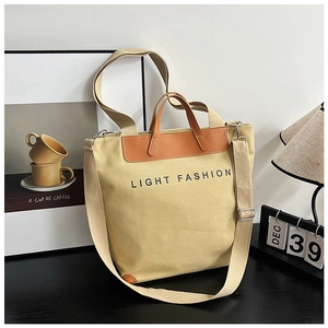 Detail of beige canvas tote bag with brown leather corners and adjustable strap
