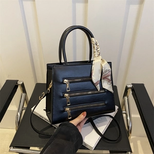 Detail view of black PU leather handbag with triple zippers and silk scarf handle