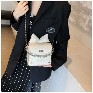 Detail of white textured mini crossbody bag featuring a large bow and silver chain strap
