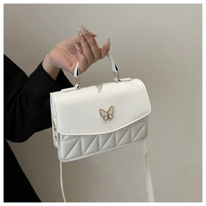 Detail of white quilted crossbody bag featuring a decorative butterfly metal clasp
