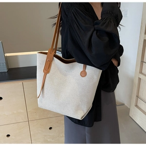 Detail of canvas tote bag with brown leather straps shown on shoulder in warm interior