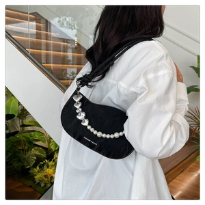 Detail of crescent shoulder bag with metallic heart and pearl chain on white shirt