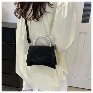 Detail of crossbody bag featuring textured black leather and white pearl handle
