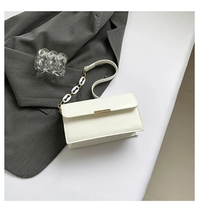 Detail of white rectangular shoulder bag with golden metal lock and acrylic chain strap