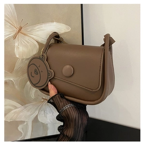 Détail du sac besace marron foncé avec boucle ronde et charmant pendentif ours