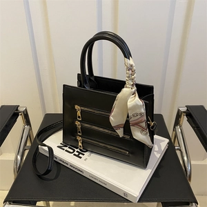 Detailed shot of black leather handbag with gold zippers and a decorative silk scarf