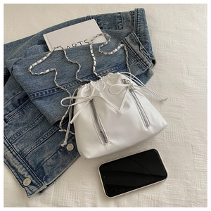 Detail view of white leather bucket bag featuring silver zippers and bow drawstring