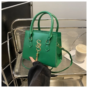 Detail of green trapezoid handbag with gold S-shaped metal ornament and fringe tassel