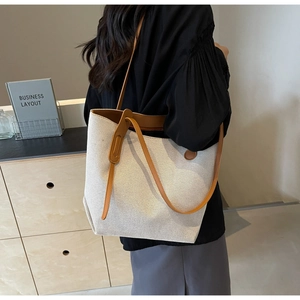 Detail of canvas tote bag showing brown leather shoulder straps and textured cream fabric