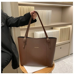 Detail of dark brown faux leather tote bag featuring gold buckle and logo on wooden stool
