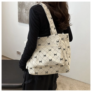 Detail of corduroy tote bag showing bow patterns and front zipper pocket on model