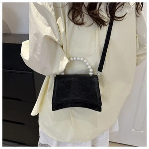 Detail view of black hourglass bag with pearl handle on model in indoor setting