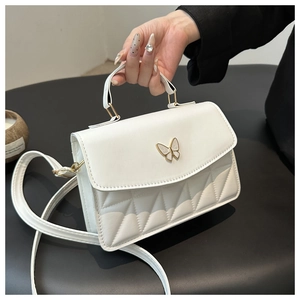 Detail of white quilted crossbody bag featuring a gold bow clasp and PU leather texture
