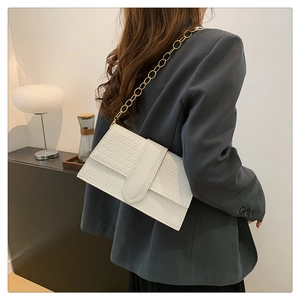 Close-up of white flap handbag featuring woven geometric texture and gold chain strap