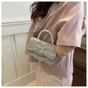Detail of silver bow bag featuring a pleated metallic finish and elegant pearl handle