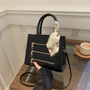 Detail of black faux leather handbag featuring golden zippers and silk scarf handle
