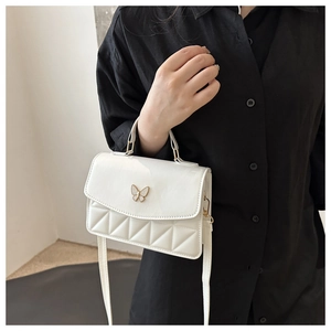 Close-up of white crossbody bag with quilted pattern and metal butterfly clasp detail