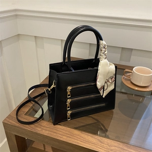 Detail of black satchel with parallel gold zippers and silk scarf handle decor
