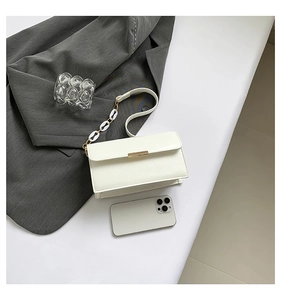 Detail of white shoulder bag with golden lock and chain strap on a blazer background