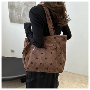 Rear view of a model wearing the brown corduroy tote bag with black bow print and quilting