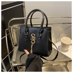 Detail of black square tote bag featuring golden SS logo, tassels and detachable strap