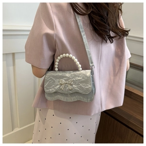 Detail of silver pleated mini bag with pearl handle and metallic bow accent