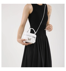 Detail of white quilted mini box bag with silver butterfly clasp and chain strap